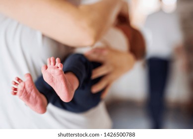 A mother holding a newborn baby at home, bare feet in the foreground.