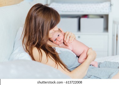 Mother Holding Newborn Baby And Lying On The Bed In Cozy Room. Side View. Child Parenting Love Concept