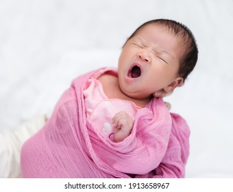 mother holding sleepy newborn baby yawning in her arm