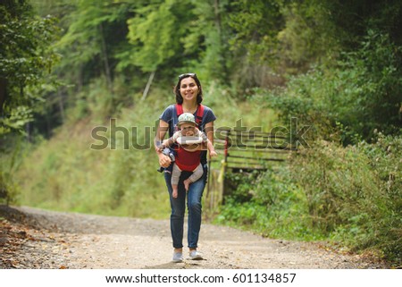 mother holding son in sling and walking in park