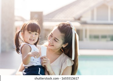 Mother Holding Sun Screen Cream Tube With Her Daughter Near Swimming Pool.Happy Mother Applying Sun Cream To Little Adorable Kid Girl.Sunscreen Or Sunblock And Skincare Concept.