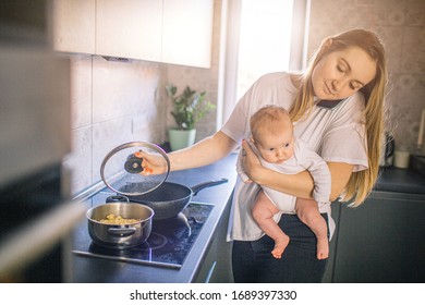 Mother Holds Her Baby In Her Arms. And Cooks In The Kitchen. Mom Speaks On The Phone And Is Very Busy. Multifunctionality Concept.