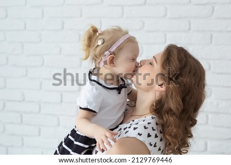 Mother holds her child with hearing aids and cochlear implants on white brick wall . Deaf and health concept