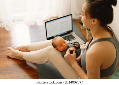 Mother holds her newborn baby son and works at the computer at home. - Powered by Shutterstock