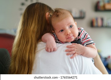 Mother holds her two moths old baby on the shoulder at home - Caucasian woman with her newborn child after feeding waiting to burp - Affectionate and bonding childhood and motherhood concept