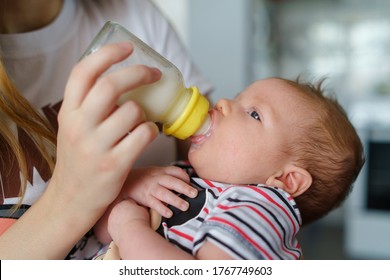 Mother holds her two moths old baby on the chair taking care at home - Caucasian woman with her newborn child bottle feeding milk on lap - Affectionate and bonding childhood and motherhood concept - Powered by Shutterstock