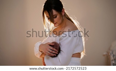 Mother holds newborn baby in her arms and gently strokes it. Woman admires child. Beautiful happy loving mom. Childhood. Concept of fatherhood. Guardianship and care of their offspring