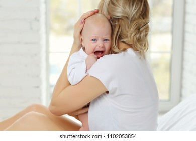 Mother holds and soothes crying baby in white clothes. - Powered by Shutterstock