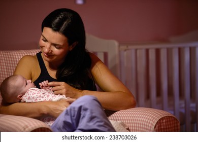 Mother At Home Cuddling Newborn Baby In Nursery