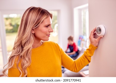 Mother At Home With Son Adjusting Smart Central Heating Thermostat Control
