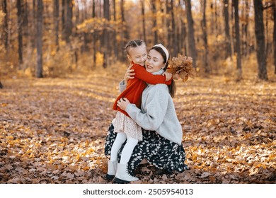 Mother is hugging her daughter with braids in an autumn forest. The woman, dressed in a gray sweater and skirt, is hugging her little daughter, who is wearing a red sweater, in the autumn forest. - Powered by Shutterstock