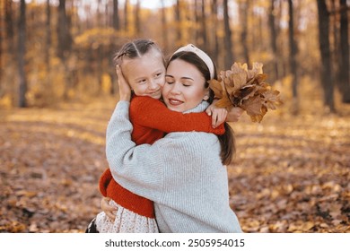 Mother is hugging her daughter with braids in an autumn forest. The woman, dressed in a gray sweater and skirt, is hugging her little daughter, who is wearing a red sweater, in the autumn forest. - Powered by Shutterstock