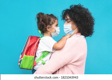 Mother hugging her daughter going back to school - Family people wearing face masks - Preschool during coronavirus concept - Main focus on mom face - Powered by Shutterstock