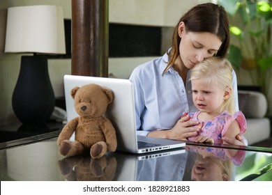 Mother Hugging Her Sad Little Girl In Front Of Laptop. Unhappy Daughter Sitting In Her Mother's Lap.