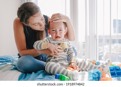 Mother Hugging Pacifying Sad Upset Crying Toddler Boy. Family Young Mom And Crying Baby Sitting On Bed At Home. Bonding Relationship Of Mom And Child Baby. Family Together Protection.