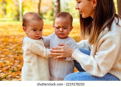 Mother Hugging Sad Twin Toddlers In Autumn Park