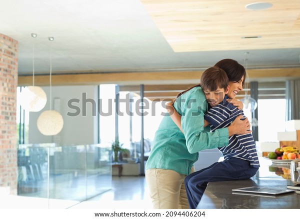 Mother hugging son in\
kitchen