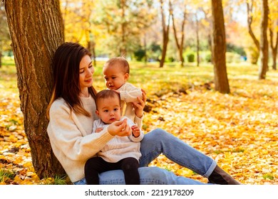 Mother Hugging Twin Toddlers In Autumn Park