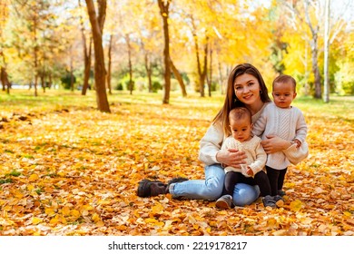 Mother Hugging Twin Toddlers In Autumn Park