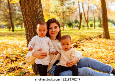 Mother Hugging Twin Toddlers In Autumn Park