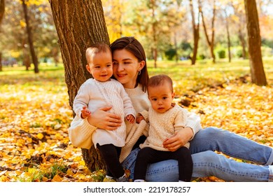 Mother Hugging Twin Toddlers In Autumn Park