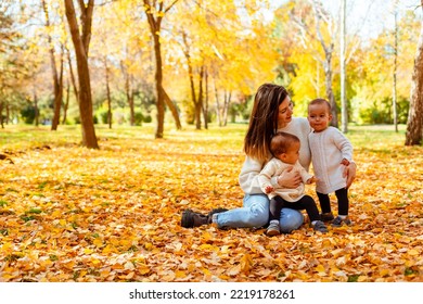 Mother Hugging Twin Toddlers In Autumn Park