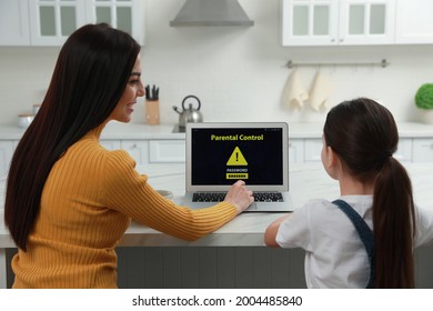 Mother Installing Parental Control On Laptop In Kitchen, Back View. Child Safety