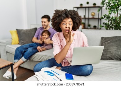 Mother of interracial family working using computer laptop at home hand on mouth telling secret rumor, whispering malicious talk conversation  - Shutterstock ID 2033978591