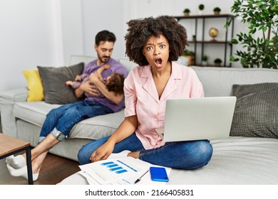 Mother Of Interracial Family Working Using Computer Laptop At Home In Shock Face, Looking Skeptical And Sarcastic, Surprised With Open Mouth 