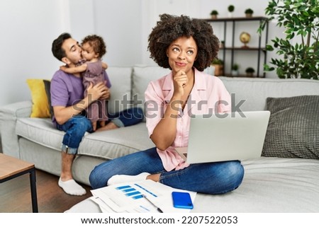 Mother of interracial family working using computer laptop at home with hand on chin thinking about question, pensive expression. smiling and thoughtful face. doubt concept. 