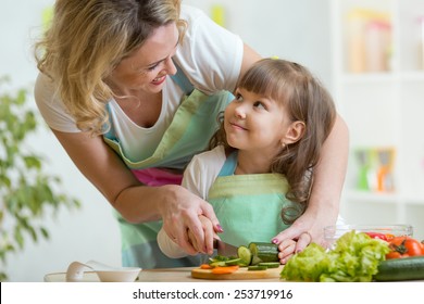 Mother And Kid Girl Cooking And Cutting Vegetables On Kitchen