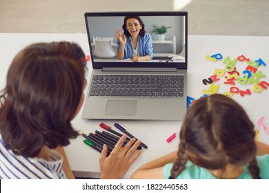 Mother And Kid Staying At Home And E-learning Via Interactive Private School Platform. High Angle Back View Mom And Daughter Video Calling Tutor On Laptop Or Having Online Lesson With English Teacher