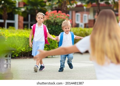 Mother And Kids After School. Young Mom Picking Up Children After Lessons In Kindergarten Or Preschool. Pick Up Students. Boy And Girl Running To Parents In School Yard.