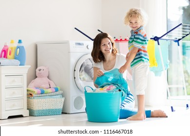 Mother And Kids In Laundry Room With Washing Machine Or Tumble Dryer. Family Chores. Modern Household Devices And Washing Detergent In White Sunny Home. Clean Washed Clothes On Drying Rack. 