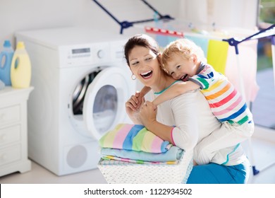 Mother And Kids In Laundry Room With Washing Machine Or Tumble Dryer. Family Chores. Modern Household Devices And Washing Detergent In White Sunny Home. Clean Washed Clothes On Drying Rack. 