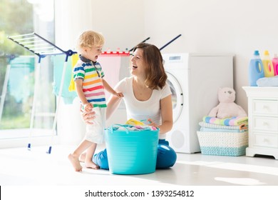 Mother And Kids In Laundry Room With Washing Machine Or Tumble Dryer. Family Chores. Modern Household Devices And Washing Detergent In White Sunny Home. Clean Washed Clothes On Drying Rack. 