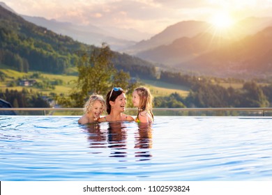 Mother And Kids Play In Outdoor Infinity Swimming Pool Of Luxury Spa Alpine Resort In Alps Mountains, Austria. Spring Or Summer Vacation For Family With Children. Kids In Hot Tub With Mountain View.