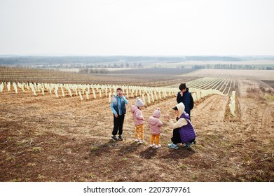 Mother With Kids Stand Against Vineyard In Early Spring.