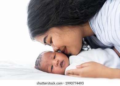 Mother Kissing Her Newborn Baby On The Bed. Closeup Of Mom And Infant Baby