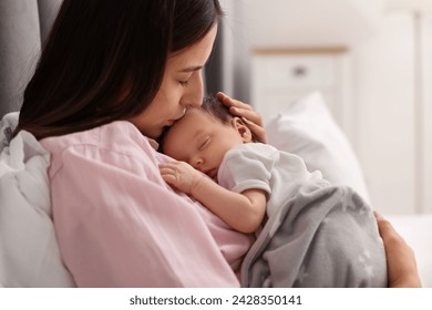 Mother kissing her sleeping newborn baby in bed at home - Powered by Shutterstock