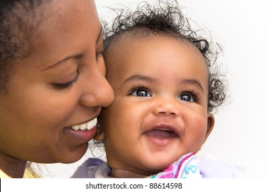 A mother kissing her smiling baby girl on the cheeks