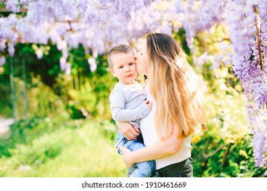 Mother kissing her son on the cheek under a wysteria tree