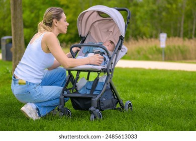 A mother kneels on the grass to adjust her baby in a stroller, enjoying a peaceful moment outdoors.