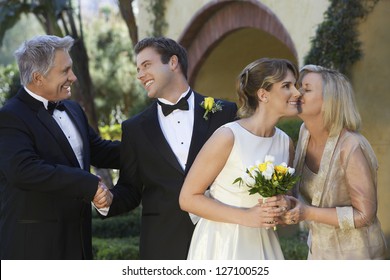 Mother In Law Kissing Bride With Happy Father And Son Shaking Hands In The Background