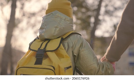 Mother Leads The Child With A Backpack On Her Shoulders, Mom Holds The Little Kid By The Hand, Lead The Baby To School, A Girl With A School Bag Walks Through The Schoolyard To A Lesson, Happy Family