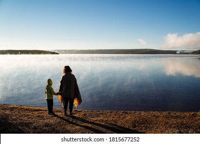 A Mother Leads Her Son By The Hand Along The Lake Shore, A Family Walk Along The River Bank, Meet The Dawn In Nature By The Water, The Silhouette Of People In The Open Air.