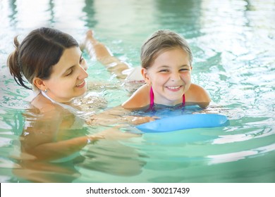 Mother Learning To Swim Her Little Daughter In An Indoor Swimming Pool. Having Fun Together. Kids Swimming Concept.