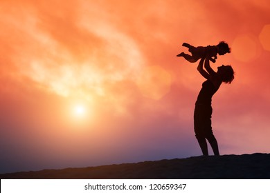 Mother lifting toddler child in air over scenic sunset sky