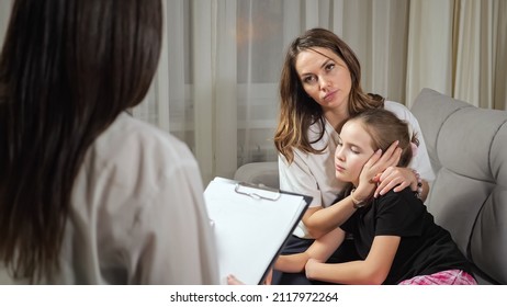 Mother Listens To Private Doctor Prescribing Medication For Sick Teen Daughter With Cold Sitting On Sofa In Living Room At Home Close View.