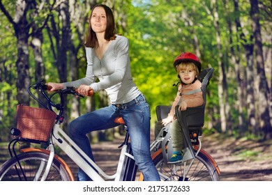 Mother with little blond boy on e-bicycle on backseat on the alley in the park